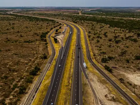 A white tractor-trailer and a few cars on a divided highway crossing flat West Texas scrubland, seen from the air