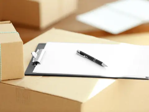 A clipboard holding a printed form with a pen lying on it, resting on top of a cardboard box