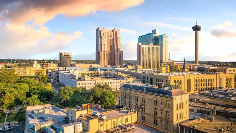 Downtown San Antonio seen from above in late-day sun, with the Tower of the Americas rising beside the hotel towers