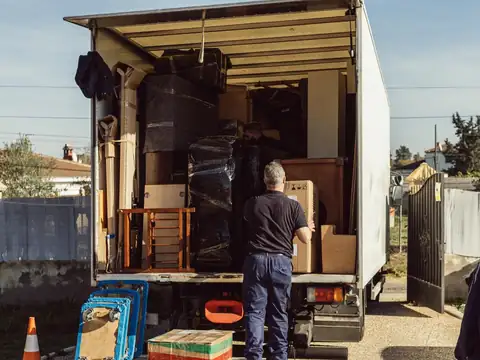 A mover seen from behind sets a carton into an open box truck packed with furniture wrapped in moving pads and stretch film