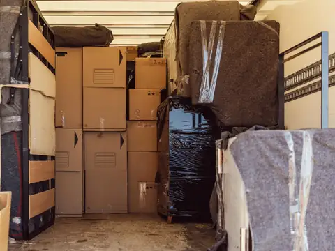 Furniture wrapped in grey moving pads and black stretch film, stacked with cartons inside a box truck
